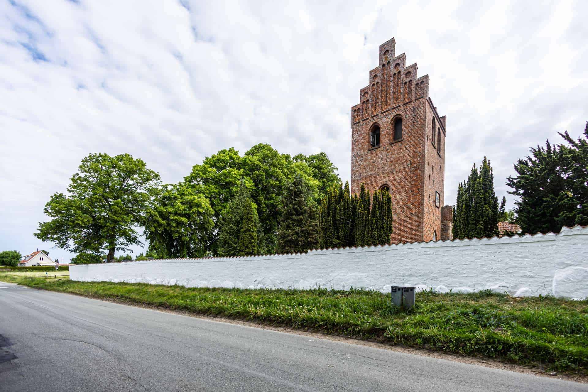 Rød kirke tårner sig op bag en nymalet hvid mur, som Murerfirmaet Hjort Jensen ApS har renoveret.